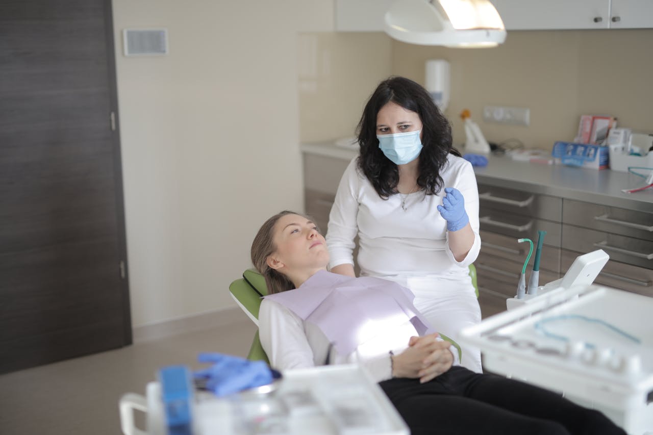 A dentist in a mask discusses treatment with a female patient in a modern dental clinic.